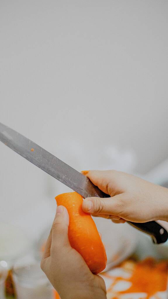a hand peeling a carrot with a knife