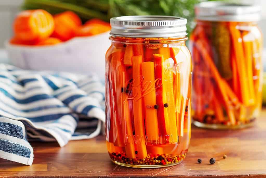 glass mason jars filled with pickled carrots, vibrant orange sticks in clear brine with spices