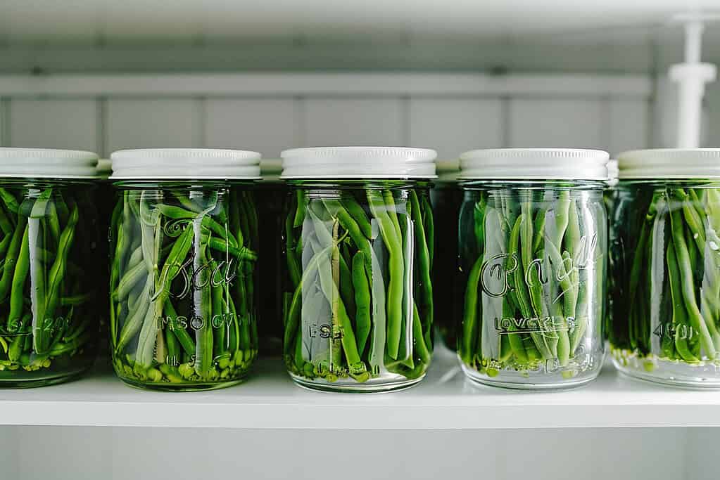 Glass jars of crisp pickled green beans neatly stored on a clean white pantry shelf