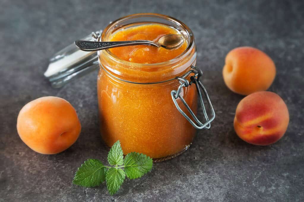 Jar of apricot jam with spoon on grey table