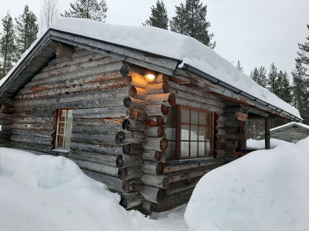 Small log cabin surrounded by deep snow in winter