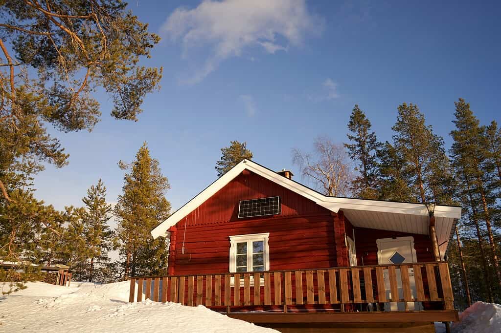 A charming, rustic red cabin nestled amidst snow-laden Norwegian pines