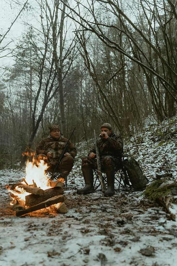 Two men sitting in camping chairs beside a campfire in the woods
