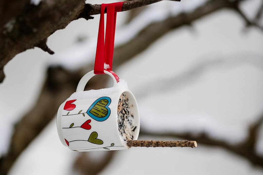 a handmade bird feeder crafted from a white ceramic teacup with colorful heart and leaf patterns