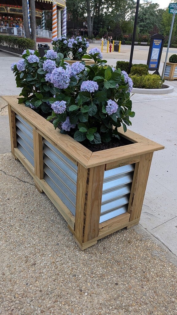 a rectangular raised garden bed made from light-stained natural wood with corrugated galvanized metal panel inserts