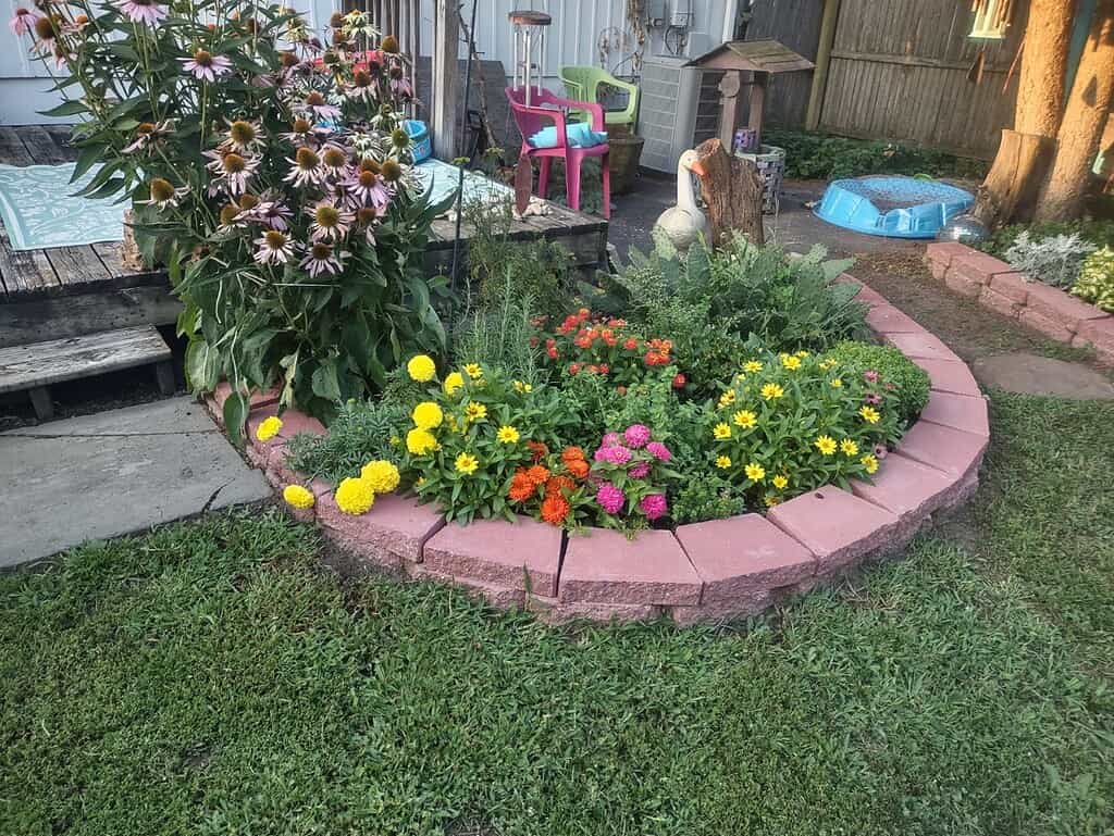 a vibrant, semi-circular backyard flower bed garden surrounded by pinkish-red concrete retaining wall blocks.