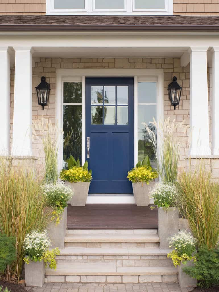 a stylish and inviting modern farmhouse entrance featuring a bold blue front door centered within a light stone façade. 