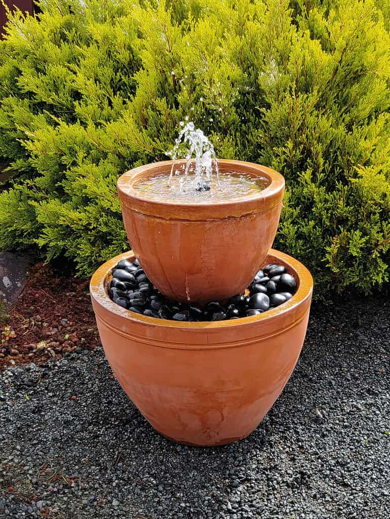 a modern terracotta garden fountain composed of two nested, smooth clay pots.