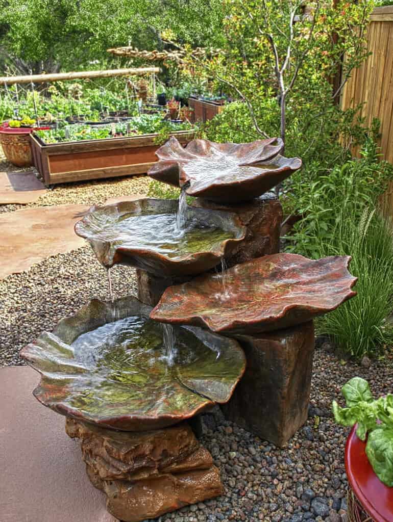 a beautifully designed backyard garden with a cascading water feature made of sculpted, large, leaf-shaped stone basins arranged vertically.