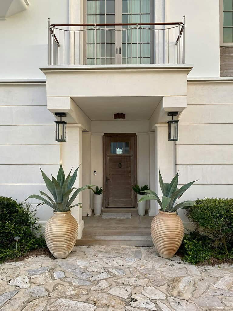 Oversized ribbed ceramic front porch planters with large agave plants flanking modern entryway with stone steps and wooden door.