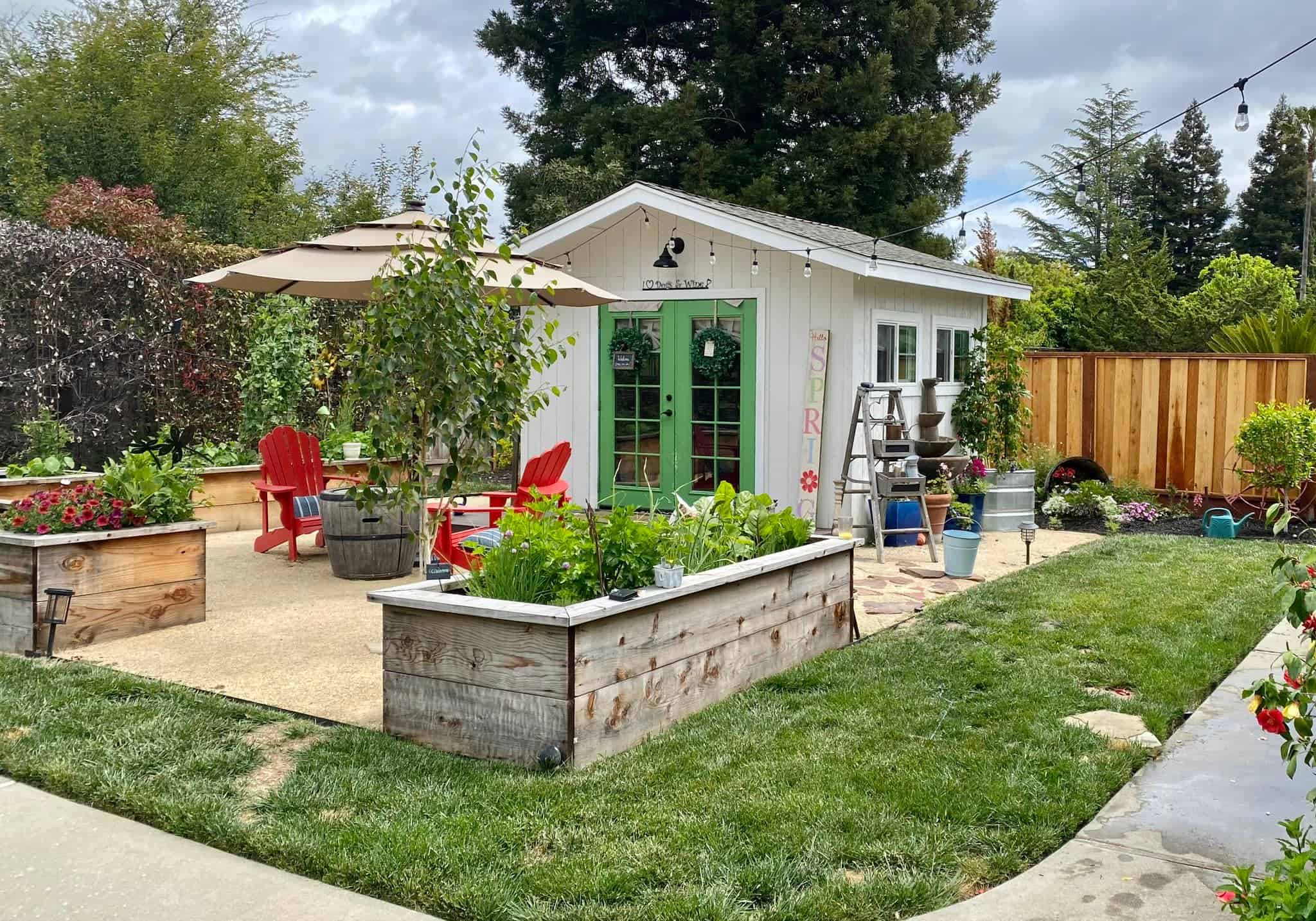 a charming white garden shed with vibrant green double French doors, styled as a cozy backyard retreat.
