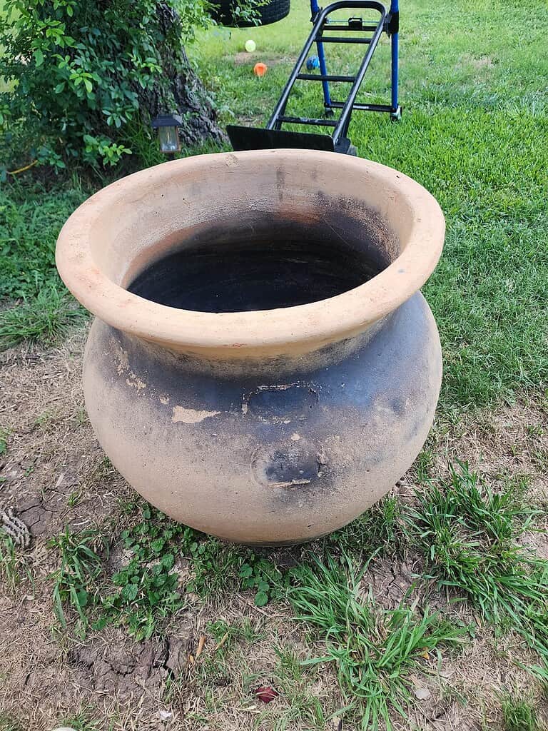 a large rustic clay cauldron-style planter placed outdoors on a grassy lawn.