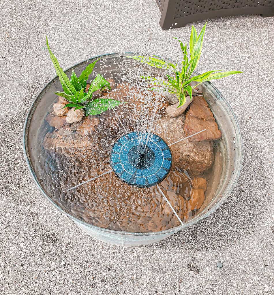 Galvanized tub patio pond fountain with floating solar pump, rocks, and small water plants.