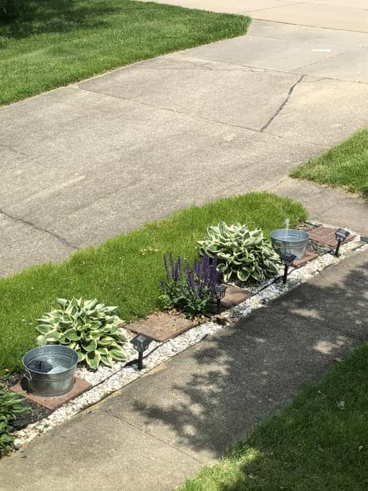 Planter pot solar fountain made from galvanized buckets along a garden pathway with solar pumps and plants.