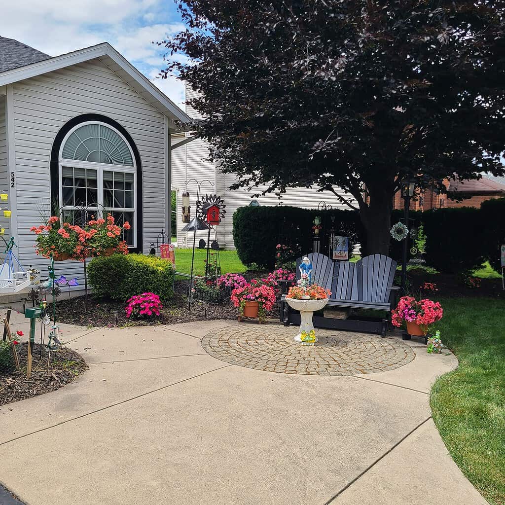 Colorful front yard garden with flowers, bird feeders, and a small patio seating area.