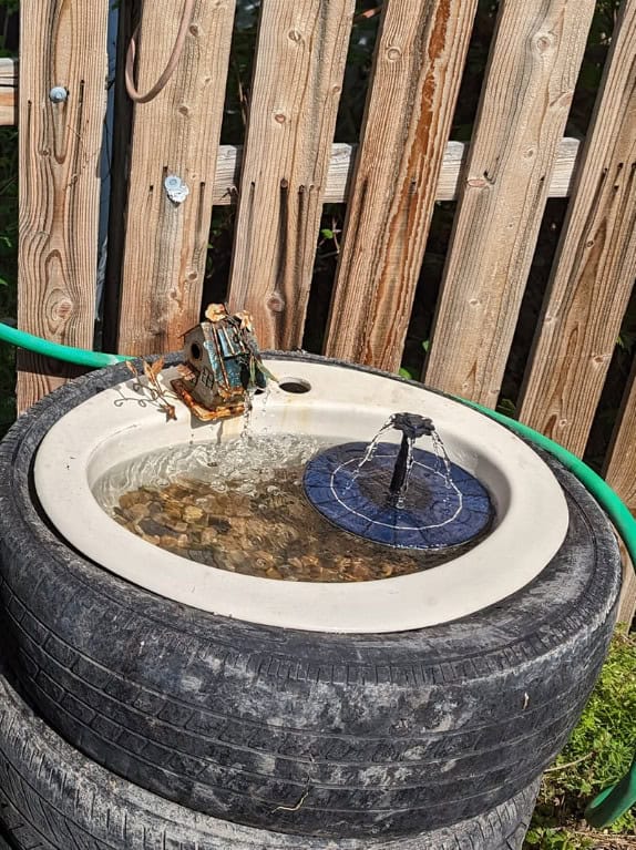 DIY solar water fountain made from a recycled tire and basin with a floating solar pump spraying water.