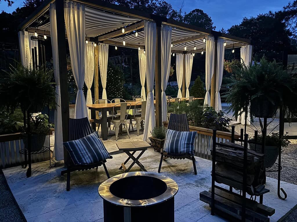 Backyard pergola with cozy seating, string lights, and fire pit creating a warm evening outdoor oasis