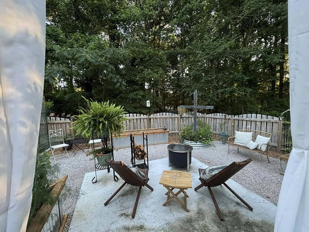 Cozy backyard seating area with fire pit, gravel ground, wooden chairs, and fenced greenery backdrop