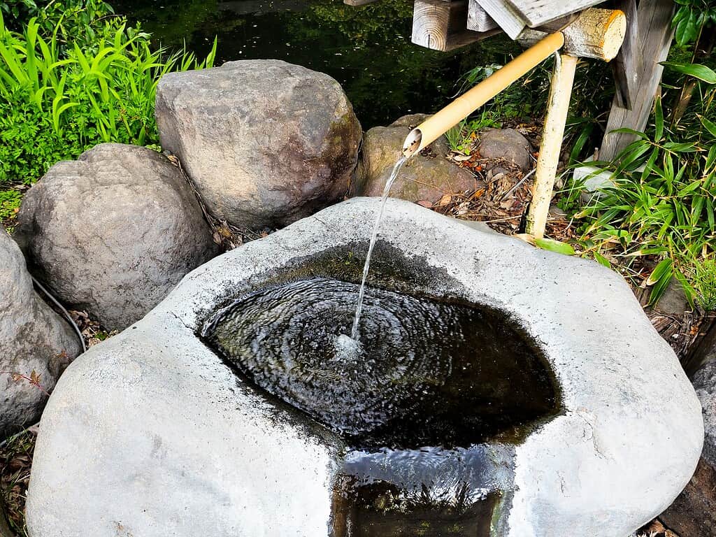 DIY pondless bubbling rock fountain with stone basin and bamboo spout in a garden.