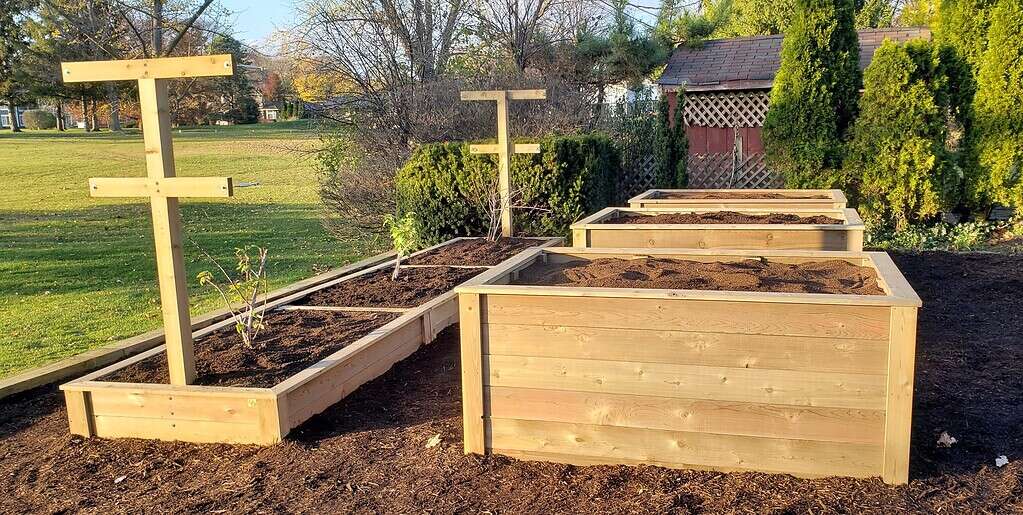 wooden raised garden beds with trellis supports filled with soil in backyard