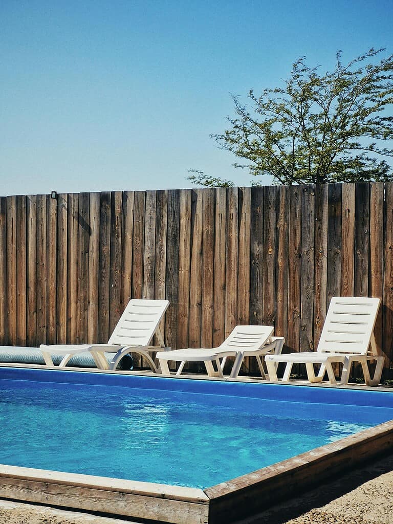 Above ground pool with lounge chairs and wooden privacy fence in backyard