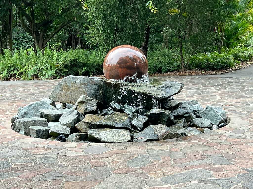 Outdoor water fountain with stone base and sphere feature in a landscaped garden walkway
