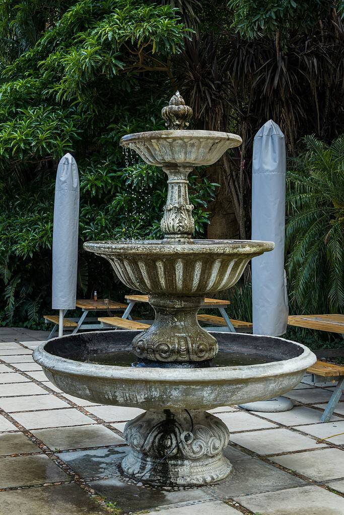 Outdoor water fountain with tiered stone design in a garden patio surrounded by lush greenery