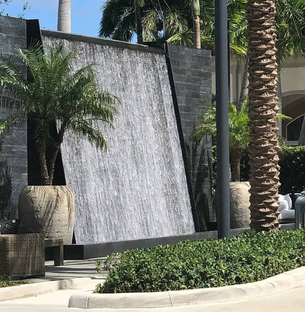 Outdoor water fountain with modern wall waterfall feature and palm trees in landscaped setting
