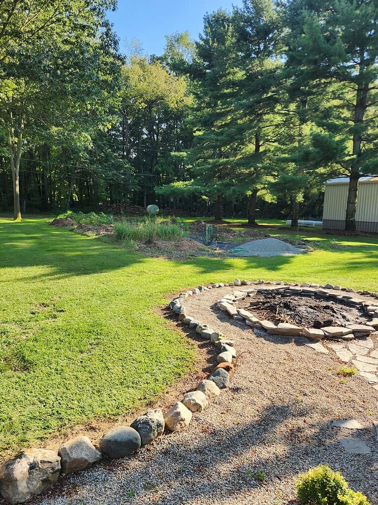 River rock landscaping around fire pit with gravel seating area and stone border in a backyard.