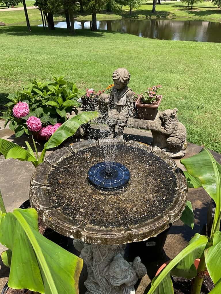 Outdoor water fountain with decorative statue and birdbath-style basin in a garden setting
