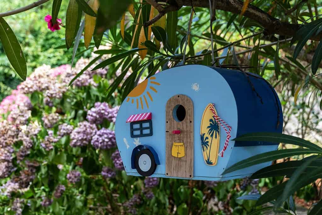 Creative DIY camper trailer birdhouse hanging in garden with colorful summer design