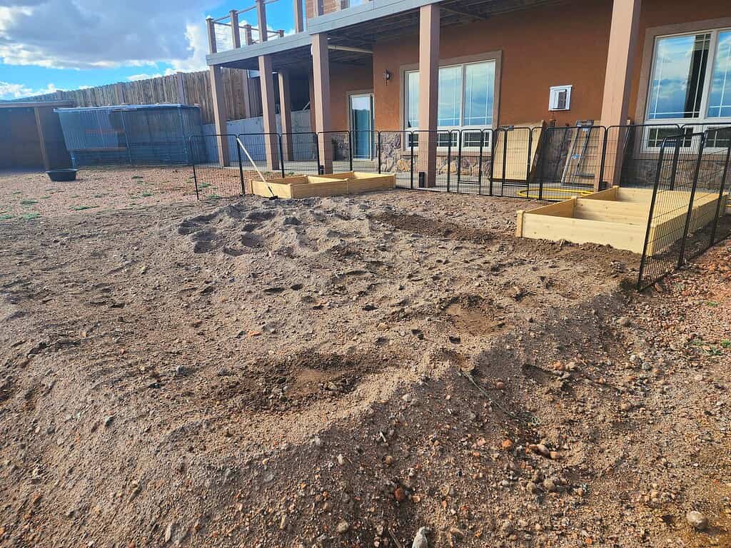 Mini-farm backyard with fenced raised garden beds and freshly prepared soil near a house
