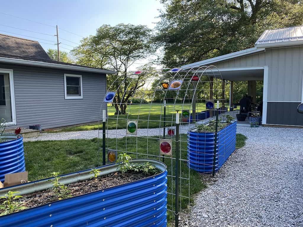 Garden trellis arch over raised beds with colorful glass accents in backyard vegetable garden