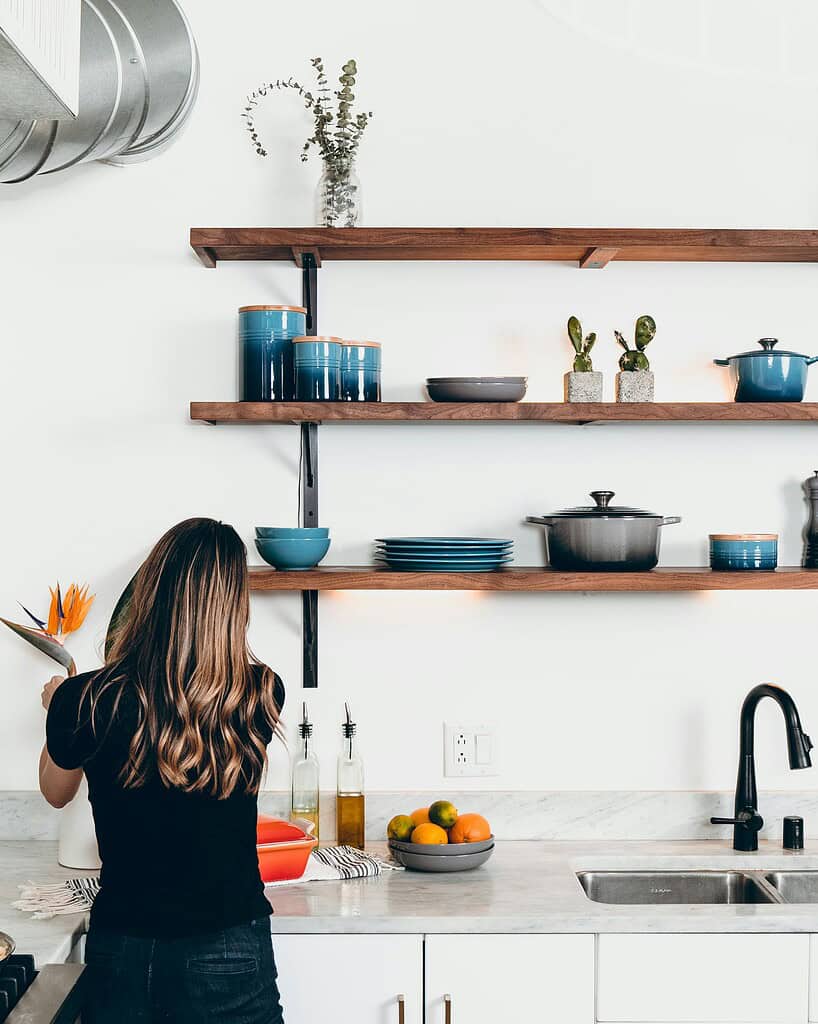 Person arranging items on a kitchen counter with shelves above.