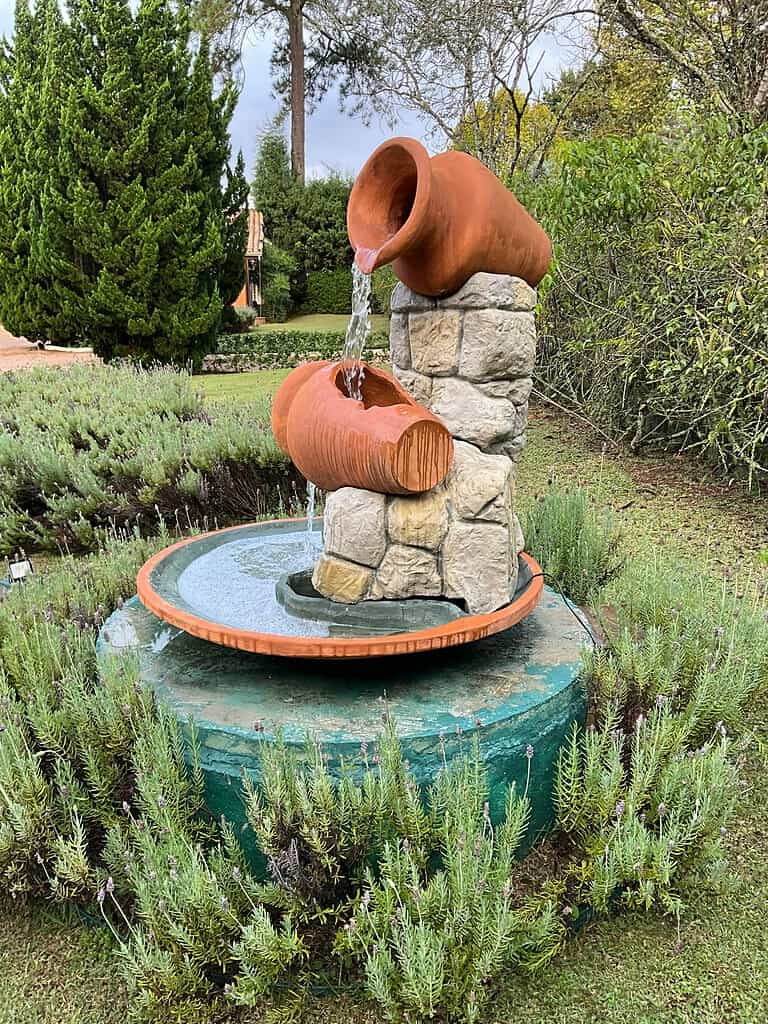 Outdoor water fountain with terracotta pots pouring water over stone base in a garden setting
