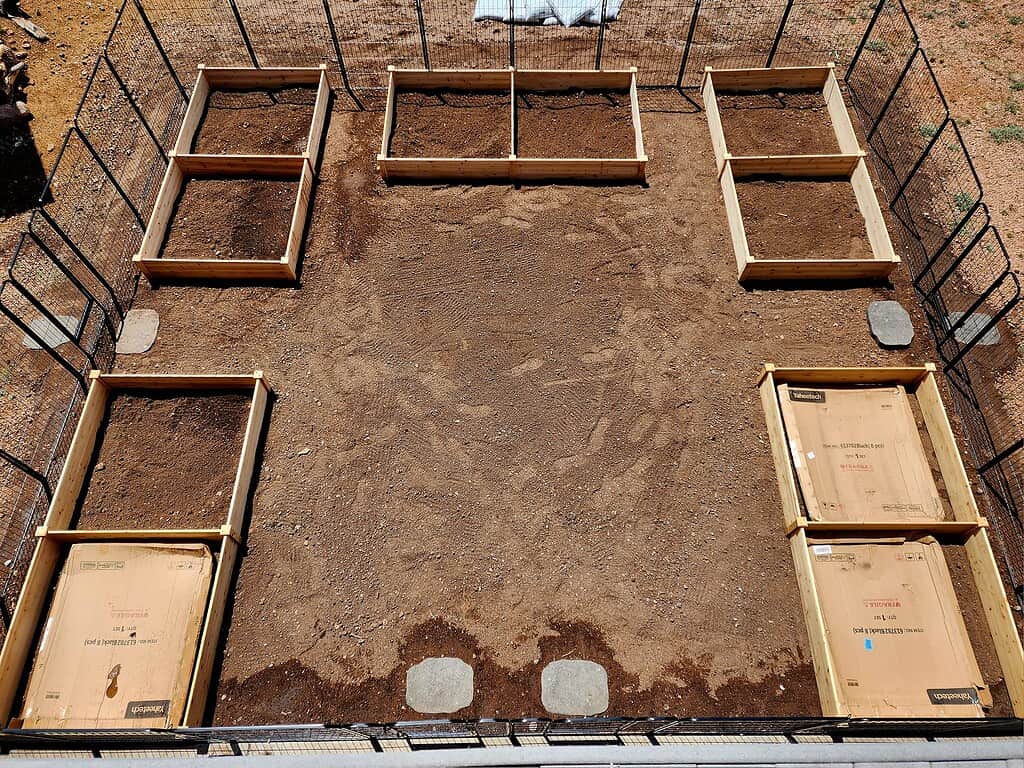 Mini-farm layout with fenced garden area and multiple raised beds filled with soil ready for planting
