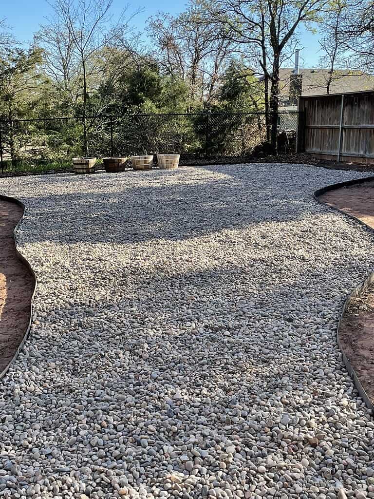 River rock landscaping with gravel yard, bordered edges, and wooden planters in a backyard setting.