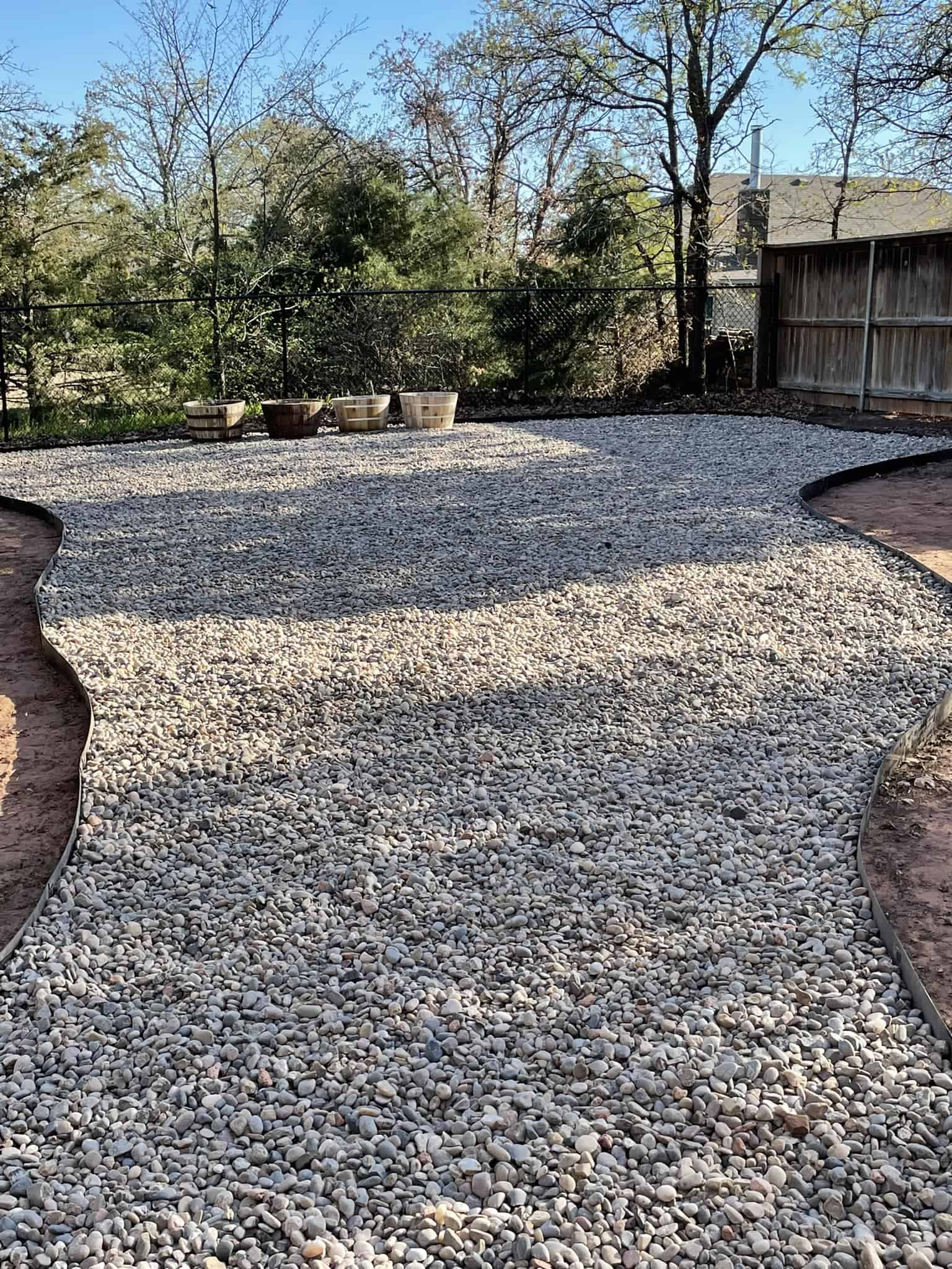 River rock landscaping with gravel yard, bordered edges, and wooden planters in a backyard setting.