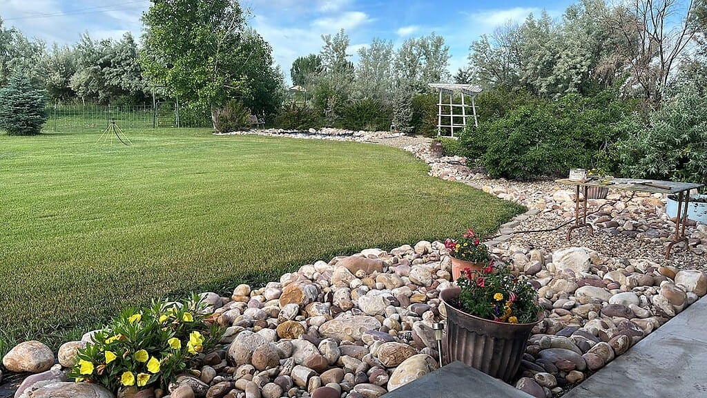 River rock landscaping border along lawn with decorative stones, plants, and garden edging.
