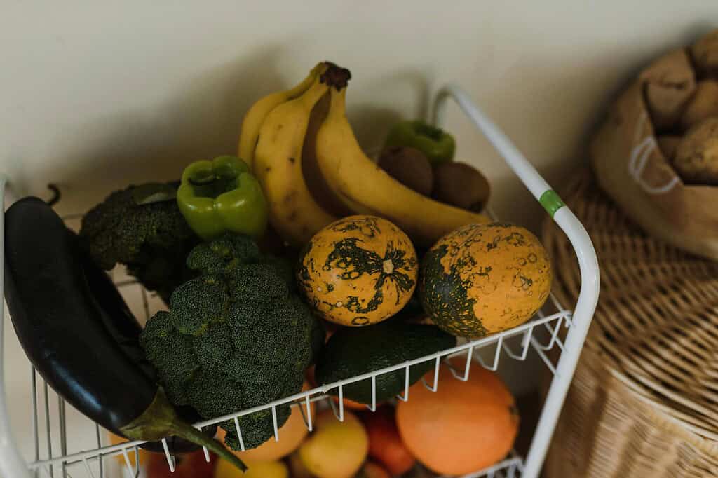 Basket of fresh produce including bananas, broccoli, peppers, squash, and eggplant.