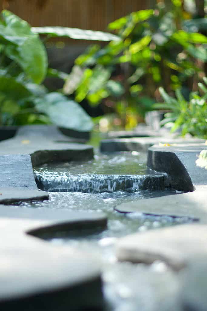 Rock garden water feature with cascading stone steps and flowing stream surrounded by lush greenery.