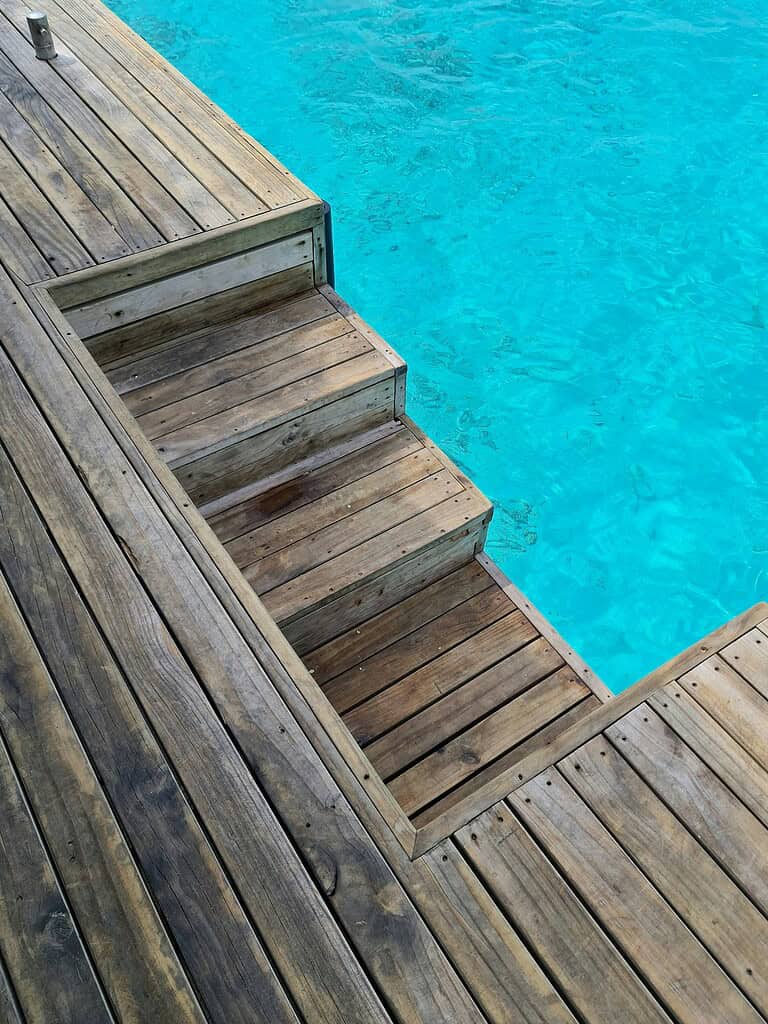 Above ground pool with wooden deck and built-in steps leading into clear blue water