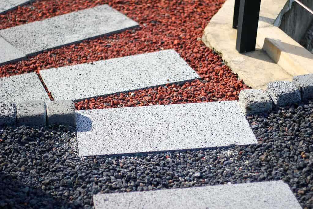 Rectangular concrete pavers set in red and black gravel forming a pathway.
