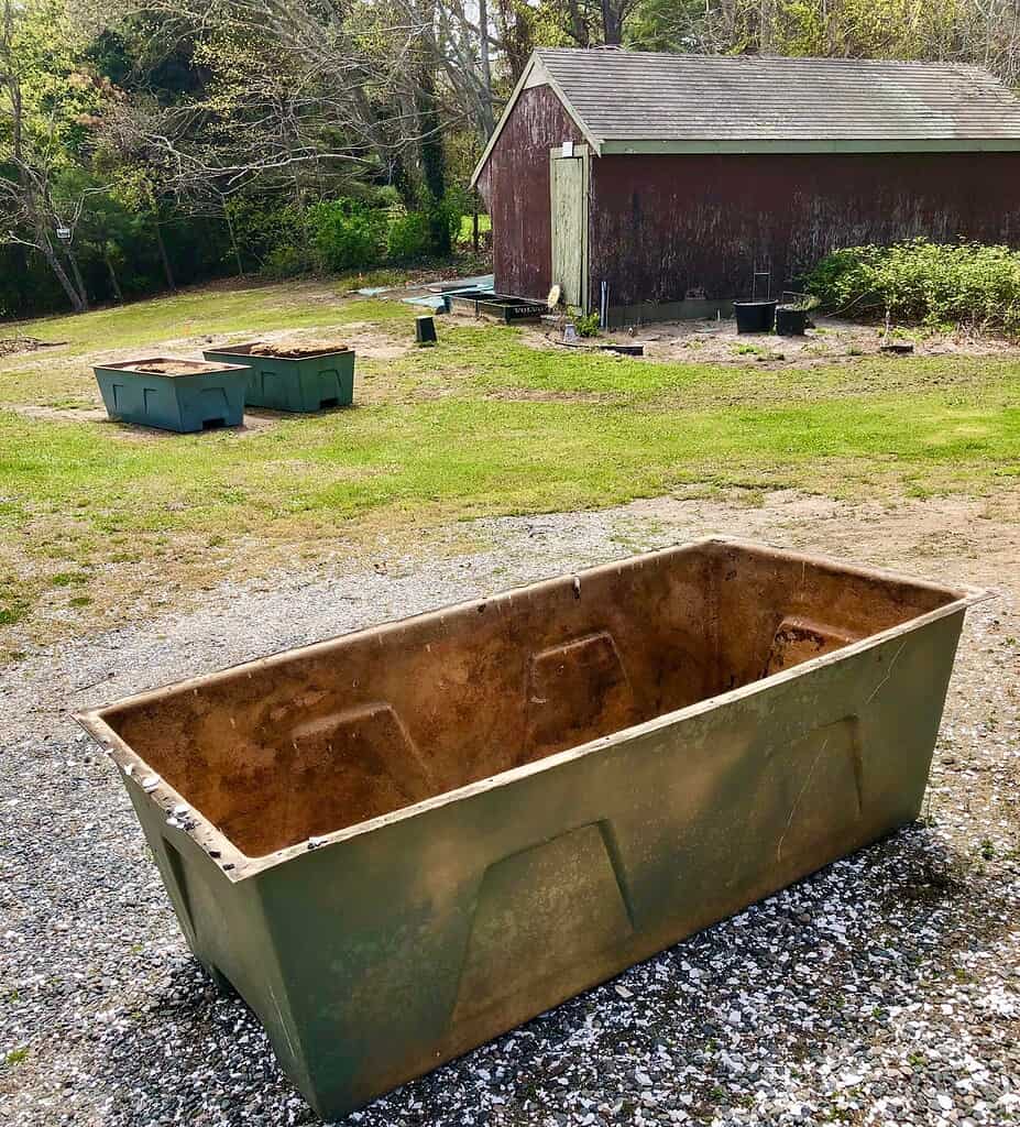 Large rectangular stock tank container on gravel ground.
