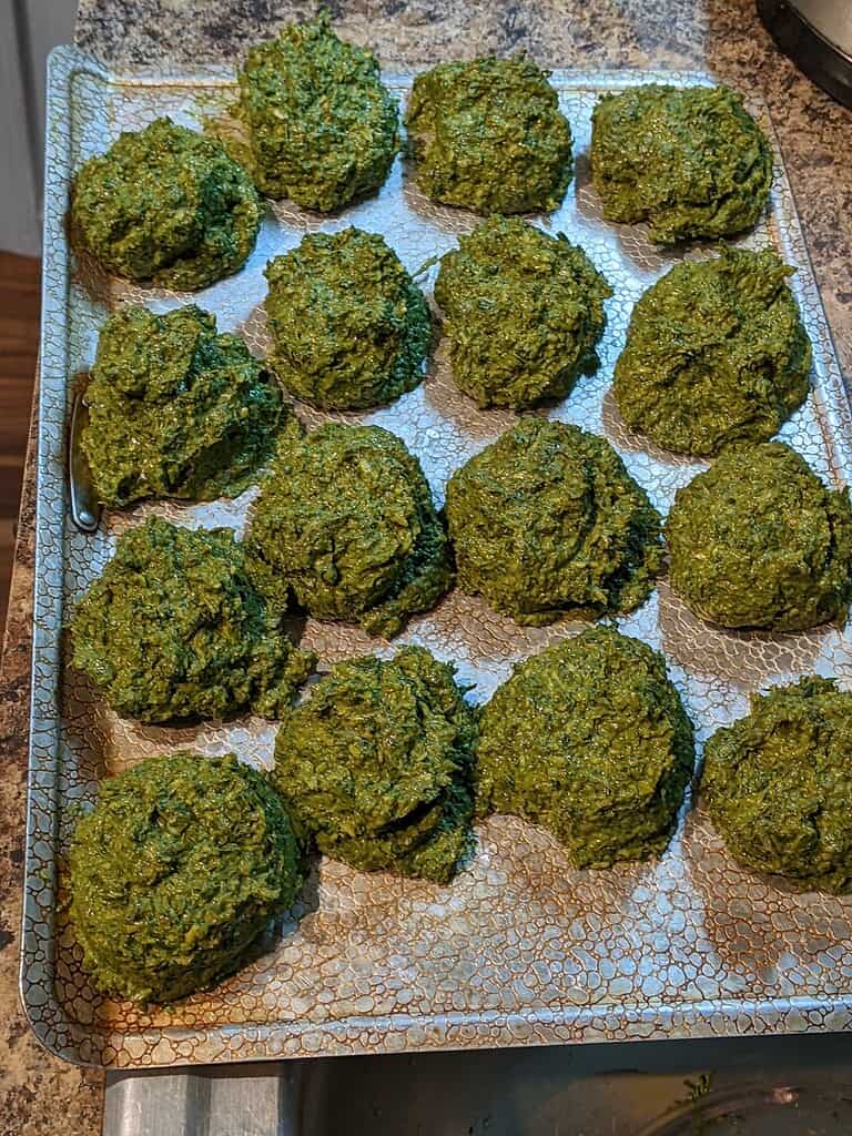 Scoops of homemade basil pesto portioned on baking tray for freezing