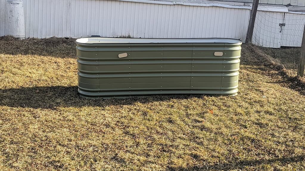 Metal raised garden bed sitting on a grassy backyard lawn.
