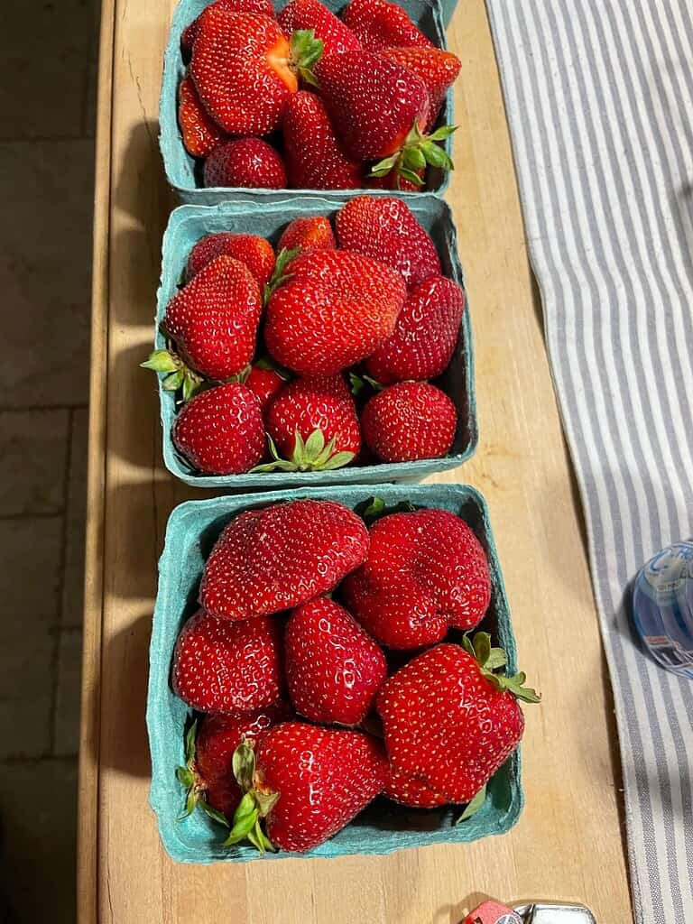 Three baskets filled with large fresh strawberries on a wooden table.